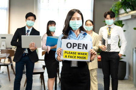 A group of office workers wearing masks. A female employee holding a sign that reads Open Please waer a face mask. Office offices that have measures to prevent viral diseases.の写真素材