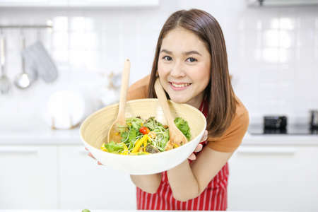 Salad in a bowl shown by Asian women in the kitchen. Woman in kitchen with various kind of vegetable.の写真素材