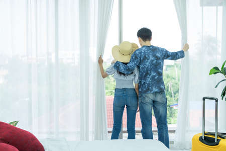 Young Asian man and women are preparing for the journey happily. Young couple relaxing In room looking out of window.の写真素材