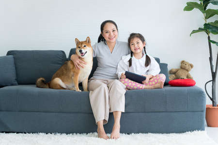 A mom and daughter is using a laptop computer and has a Shiba Inu on the sofa. Mom and baby.の写真素材