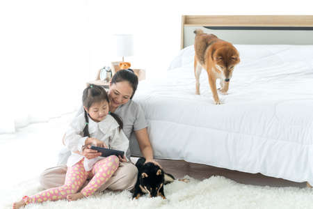 A mom and daughter is using a tablet computer and has a Shiba Inu on the sofa. Mom and baby.の写真素材
