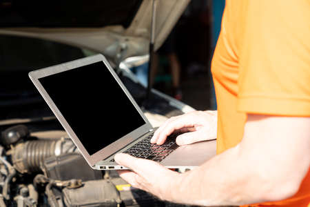 A car mechanic is using a laptop computer to check the engine operation.の写真素材