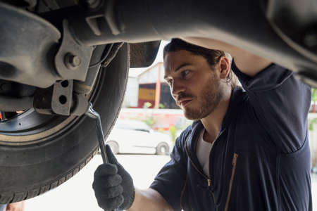 A car mechanic repairing the brakes and shock absorber. Car brake repairing in garage. Auto mechanic hands using wrench to repair a car engine.の写真素材