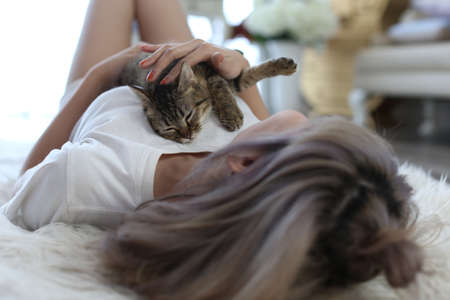 A cat is sleeping on a young Asian woman's chest in a morning-lit living room.の写真素材