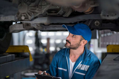 Service repair maintenance concept. Handsome worker in uniform changing car wheel. Male mechanic using rim wrench to fix car tire at auto repair shop.の写真素材