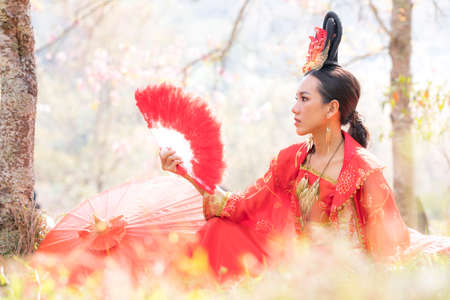 Chinese girl wearing Ancient chinese dress or Cheongsams dress Traditional Chinese dress, Young woman holding a fan and a red umbrella.の写真素材