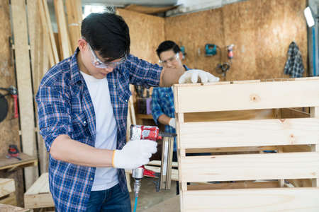Carpenter hammering nails into wood with a automatic nailer. Carpenter worker with machine at wood workshop.の写真素材