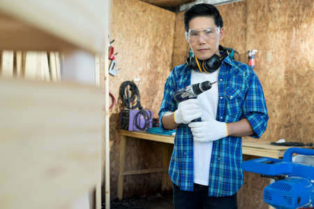 Carpenter Drilling Wood. Young carpenter man in hardhat drilling wood in working studio.