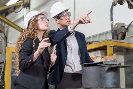The engineer is explaining the operation of the machine to the manager. Man and woman talking and using tablet computer with robot arm production line.の写真素材