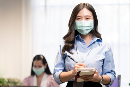 Employees who are recording the meeting. A young worker wearing a mask in the office.の写真素材