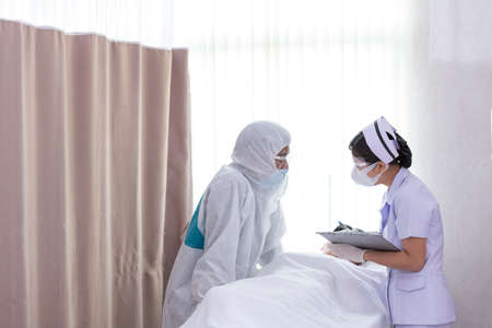 Doctor talking to nurse.  Doctor and nurse with full body cover suit discuss and help Covid-19 infected patient in close room.の写真素材