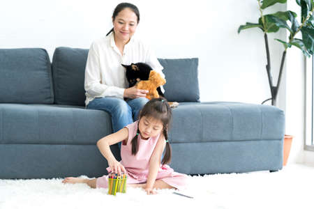 A mother teaching her daughter to paint in a living room with a Shiba Inu dog. Mother teaching her...