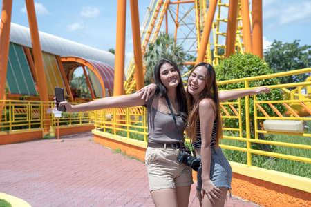Teenage girls traveling in an amusement park. Two female are taking pictures of themselves in an amusement park.の写真素材