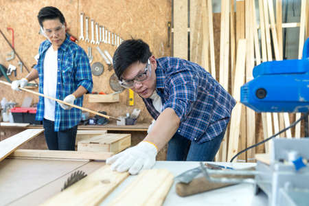Craftsmans working together at carpentry shop. Carpenter working with circular saw at carpentry workshop.の写真素材