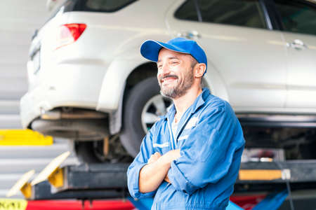 The car mechanic is smiling proudly in the auto repair center. Happy auto mechanic man or smith at car workshop.の写真素材