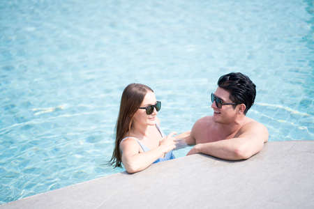 Man and woman in a swimming pool. Young couple embracing in the pool. Beautiful female happy doing exercise and working out.の写真素材