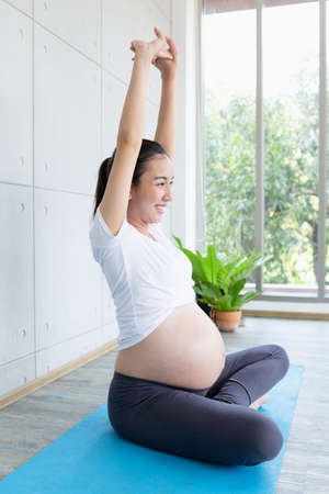 Mom is having fun doing yoga. Pregnant woman doing morning exercises at home.の写真素材