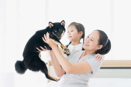 A family with a mother and daughter holding black Shiba Inu dog in bedroom.の写真素材