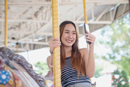 Young woman taking selfie on carousel in amusement park. Attractive women taking selfie in amusement park.の写真素材