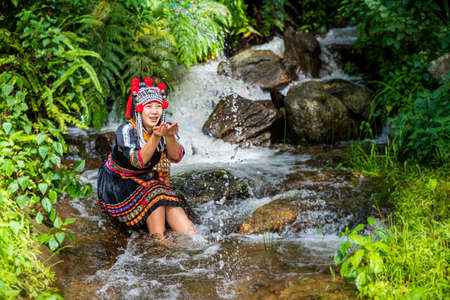 Hmong hill tribe clothes. A young hill tribe woman is playing in the water on the waterfall.の写真素材