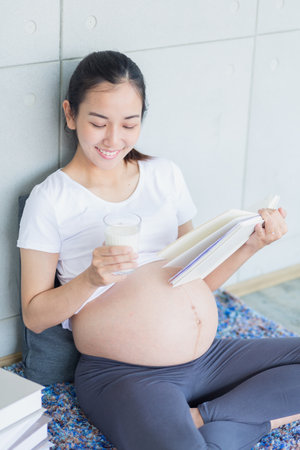 Pregnant is having fun doing yoga. pregnant woman drinking milk and reading in the living room.の写真素材