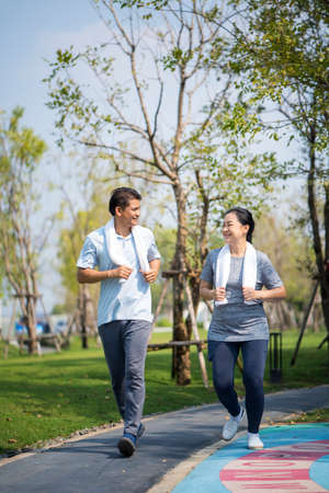 Asian mature man and woman running outdoors. Happy mature couple in summer sports running outfit.の写真素材