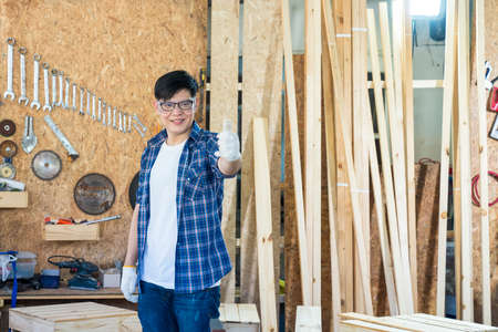 Carpenter showing thumb up. Young male carpenter working wood workshop.の写真素材