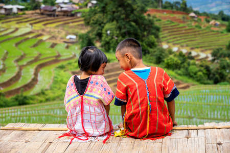 A boy and a girl dressed in hill tribe clothing are sitting on the terraced rice fields. A Hmong farmer looking at the terraced rice fields.の写真素材