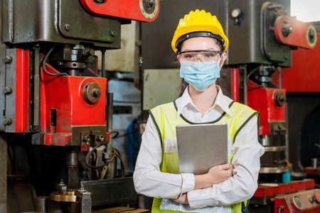 Asian woman wearing a mask holding a tablet in an industrial factory. Professional technicians are holding a tablet to control work in industrial plants.の写真素材
