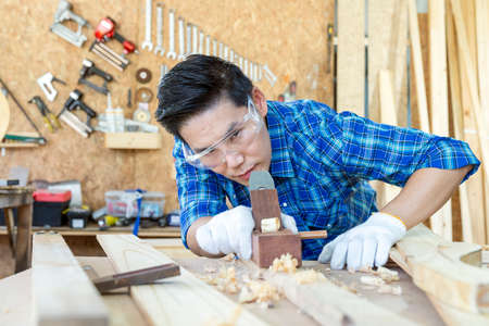 A carpenter is using a wood sharpener. Carpenter builder handles a wooden plank board plane in the workshop.の写真素材