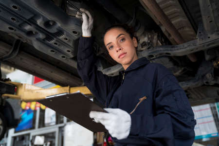 Service repair maintenance concept. African American woman work for auto mechanic in garage checking car engine.の写真素材