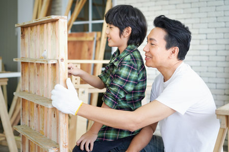 The Boy is learning to work on wood. Father and son working with wood plank in workshop. Father and son painting on wood.の写真素材