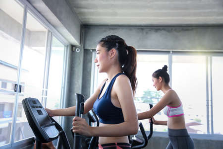 Female are committed to exercise. Young female working out on elliptical trainer in modern gym.の写真素材