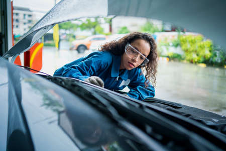 African American woman work for auto mechanic in garage checking car engine. A car mechanic is changing the oil in a car repair workshop.の写真素材