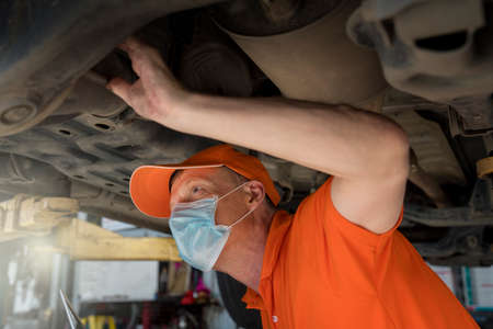 Service repair maintenance concept. A car mechanic wearing a mask is holding a laptop to check the car's performance.の写真素材