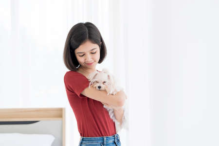 A young Asian woman holding a white Maltese puppy in her bedroom. Girl and puppy dog.の写真素材