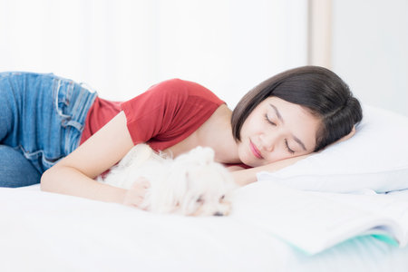 Pet Lover. A young Asian woman sleeping with puppy Maltese dog on the bed in her bedroom.の写真素材