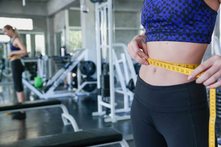 Slim woman measuring her waist at gym. Slim body woman measuring her waist at gym.の写真素材