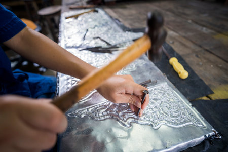 Silversmiths tools on the silver workplace. Silversmith using hammer and steel engraved pattern on...