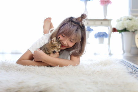 Young Asian woman hugging a cat on the floor in the living room.の写真素材
