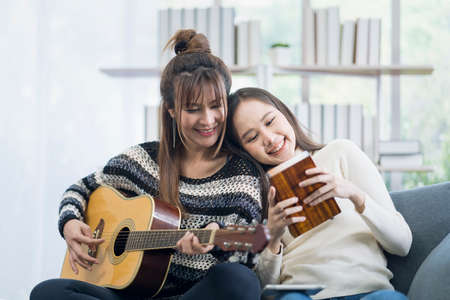 Two young lesbians are playing music. guitar and kalimba on the sofa in the living roomの写真素材