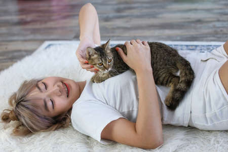 Young girl with cat on couch at home. The girl's fingers are playing with a cat lying on her chest.の写真素材