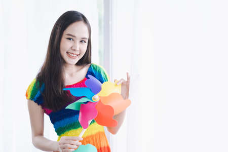Lesbian concept. Lgbt Concept. A young woman wearing a rainbow dress is holding a windmill in the living room.の写真素材