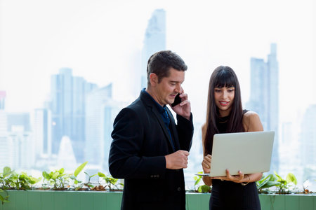 Businessman using laptop computer and mobile phone on a tall building in the office building.の写真素材