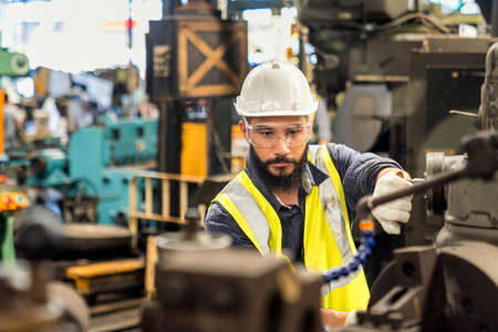 Man technician is working in a steel factory. Man worker in safety helmet working on steel machine.