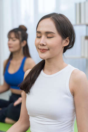 Female doing yoga exercises. Full length of two young sporty women stretching hands in fitness studio.の写真素材