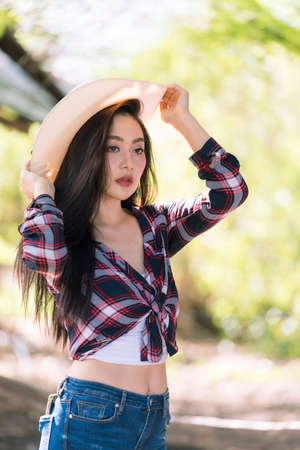 Beautiful cowgirl style model posing on farmland. Young adult Asian woman fashion in natural...