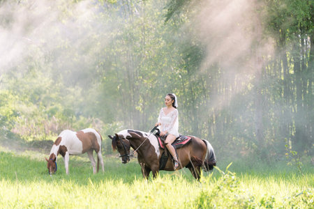 Young woman in white dress with horse. Woman riding red horse in the garden. Beautiful bride in a dress riding a horse.の写真素材
