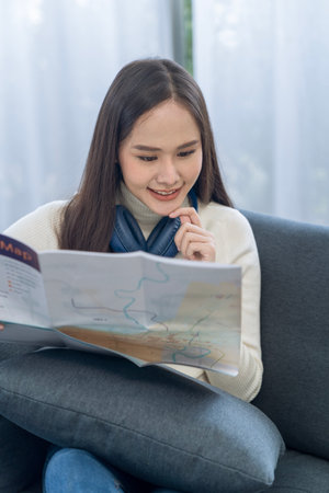 Young woman planning a trip and holding a map in the living room.の写真素材