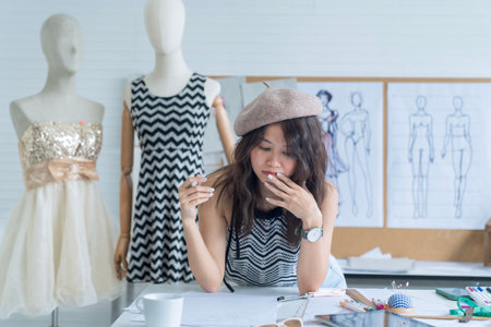 Fashion designers working in studio sitting on the desk.Young Asian designer woman stress working design creative while sitting at office studio.の写真素材